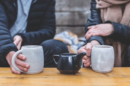 Two people holding mugs of coffee while in conversation